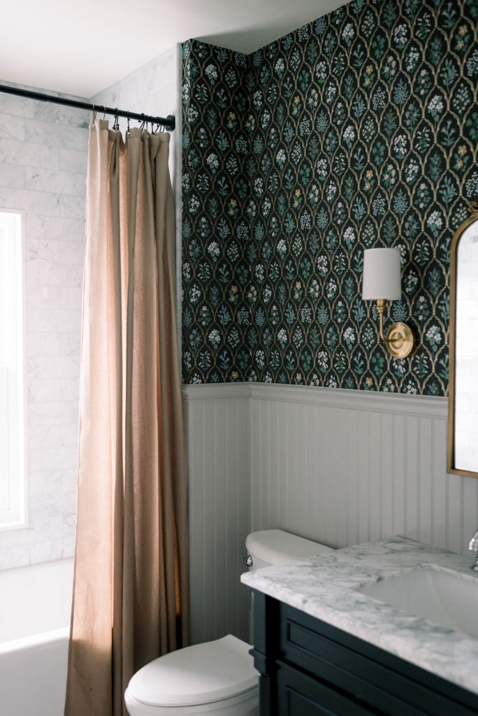 This dark marble bathroom is a stark contrast from what it was before – cramped and in need of work. The Rifle Paper Co Hawthorne wallpaper contrasts perfectly with all of the marble tile from The Tile Shop. The sconces from Signature Hardware, the antique brass mirror from Kate & Laurel, and the Farrow and Ball Purbeck Stone painted beadboard tie the whole space together.